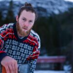 A man in a Nordic sweater stands outdoors in a snowy winter landscape.