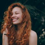 A candid portrait of a joyful woman with curly red hair, expressing natural beauty and happiness.