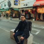 Man sitting on a stone bench in Seoul's vibrant shopping street.