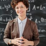 Teacher standing by a blackboard with algebra equations, smiling confidently.