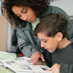 A woman helps a boy read in a classroom setting. Educational support concept.