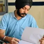 A South Asian man wearing a turban intently studies documents at a desk in India.